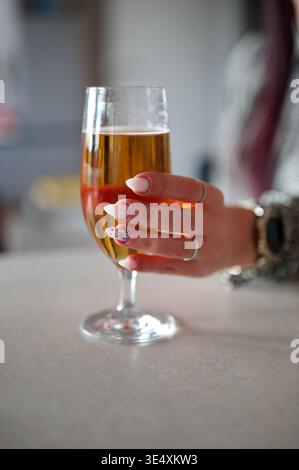 Die Hand einer Frau hält ein Glas Bier. Sie hat Nägel mit einem Osterhasen auf einer von ihnen gepflegt. Stockfoto