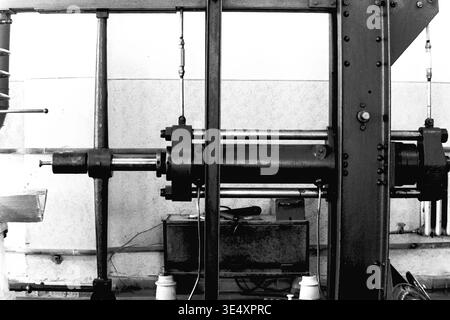 Sloviansk, 1950er-1960er Jahre, Armature-Insulator Plant (AIZ). Detaillierte Archivaufnahme einer schweren industriellen Prüfpresse, die zur Qualitätskontrolle von elektrischen Hochspannungsisolatoren verwendet wird. Das Vintage-Schwarz-weiß-Foto hebt den robusten Stahlrahmen, die Hydraulikzylinder und die komplexe Konstruktion des mechanischen Bohrgeräts hervor. Dieses Bild zeigt die strengen technologischen Standards und Qualitätssicherungsprotokolle in der sowjetischen Fertigung und bewahrt die Maschinengeschichte des friedlichen Donbas. Stockfoto