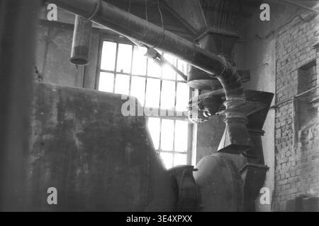 Sloviansk, 1950er-1960er Jahre, Armature-Insulator Plant (AIZ). Archivfoto einer großen horizontalen Kugelmühle, die zum Schleifen von keramischen Rohmaterialien in der Fabrik für elektrische Isolatoren verwendet wird. Das Schwarzweiß-Bild zeigt die schweren zylindrischen Maschinen und die oben liegenden Lüftungskanäle, die sich neben einer alten Ziegelmauer und in Sonnenlicht getauchten Industriefenstern befinden. Diese faszinierende mechanische Szene erfasst die grundlegenden Prozesse der sowjetischen Energietechnik und das Erbe des friedlichen Donbass. Stockfoto