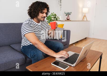 Junger Indianer trinkt Kaffee mit Laptop Stockfoto