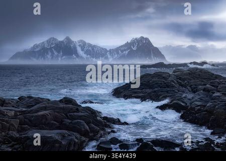 Bestaunen Sie die zerklüftete Küste von Svolvaer in Lofoten, Norwegen, wo dunkle Wellen gegen alte Felsen krachen. Stockfoto