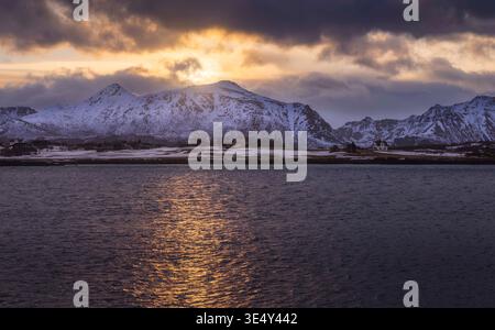 Goldenes Licht bricht über den zerklüfteten Gipfeln von Leknes und schafft einen atemberaubenden Kontrast zu den dunklen Wolken. Das ruhige Wasser reflektiert das B des frühen Tages Stockfoto
