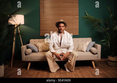 Stilvoller Mann, der auf Sofa in gemütlichem Zuhause sitzt Stockfoto