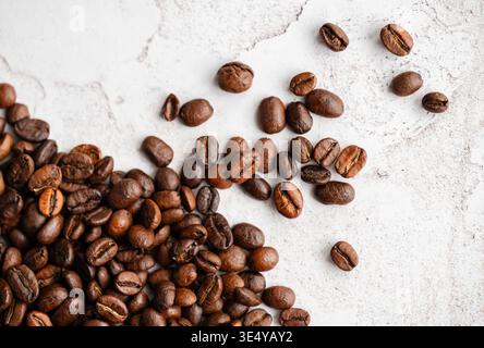 Blick von oben auf geröstete Kaffeebohnen, die auf hellem Hintergrund verschüttet werden. Stockfoto