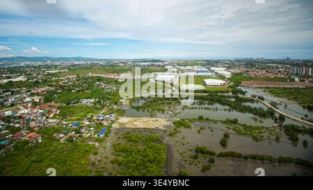 Aus der Vogelperspektive auf die üppige grüne Vegetation trifft auf die weitläufige Stadtlandschaft unter einem riesigen Himmel, Mactan, Philippinen. Stockfoto