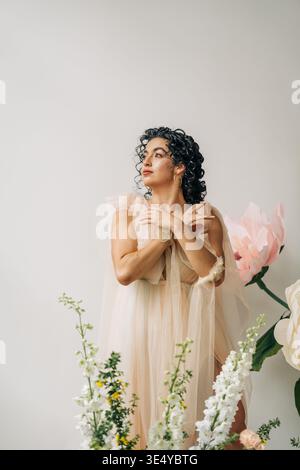Frau träumt in ätherischem beigefarbenem Kleid zwischen Blumen Stockfoto
