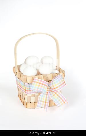 Korb voller weißer Eier, gebunden mit einem bunten karierten Osterbogen Stockfoto
