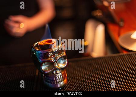 Ein Glas Schädel mit einem alkoholischen Cocktail und Verbrennungen von Passionsfrüchten an der Bar. Zombie-Cocktail Stockfoto