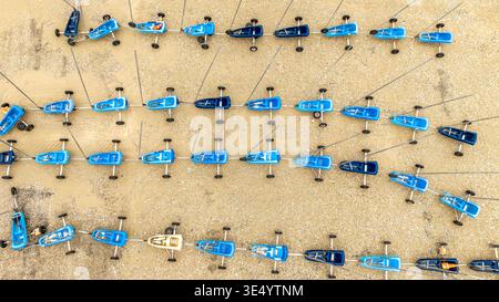 Aus der Vogelperspektive sehen Sie leuchtend blaue und weiße Sandyachten, die sich in ordentlichen Reihen aufeinanderreihen, bereit für ein Rennen am Sandstrand, Fort-Mahon-Plage, Hauts-de-France, Franc Stockfoto