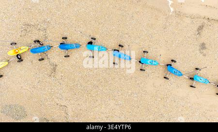 Aus der Vogelperspektive sehen Sie leuchtend blaue und gelbe Landyachten, die sich wie Juwelen am Sandstrand aneinander Reihen, Fort-Mahon-Plage, Hauts-de-France, Frankreich. Stockfoto