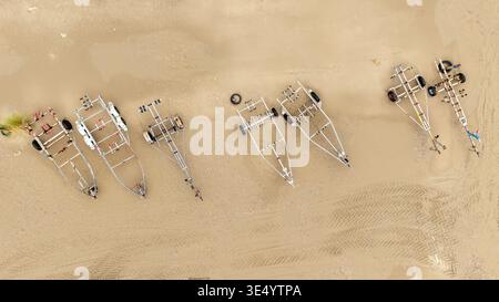Aus der Vogelperspektive sind Bootsanhänger am Sandstrand angeordnet, deren metallische Rahmen unter der Sonne glänzen, Fort-Mahon-Plage, Hauts-de-France, Frankreich. Stockfoto