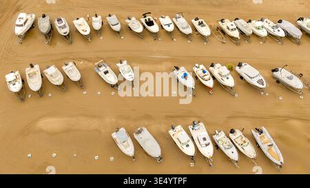 Aus der Vogelperspektive sehen Boote, die ordentlich am Sandstrand ausgerichtet sind, ein nautisches Tableau aus Rümpfen und Anhängern vor der ruhigen Kulisse von Fort-Mahon-Plage, Ha Stockfoto