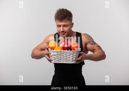 Gesunder athletischer gutaussehender Mann mit muskulösen Körper, der Obstkorb hält und schnüffelt. Gesundheit, Ernährung und Vitamine Stockfoto