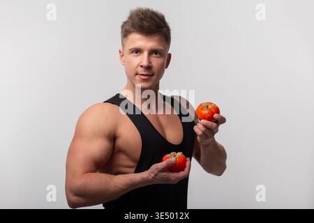 Gesunder gutaussehender athletischer starker Mann im schwarzen T-Shirt hält Persimmon im Studio. Gesunde Lebensmittel und Vitamine Stockfoto