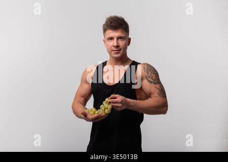 Starker athletischer, gutaussehender Mann mit muskulösem Körper, der Trauben hält. Vitamine und Früchte Stockfoto