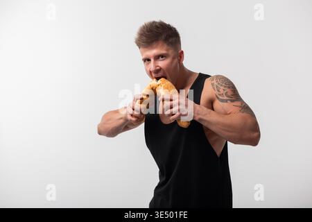 Gesunde gutaussehende athletische muskulöse Mann beißt Baguette. Ernährung und Ernährung Stockfoto