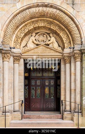 Reich geschnitzte romanische Steintür der Church of the Hidden Juwel, Manchester, mit Engeltympanon, lateinischer Inschrift und Buntglastüren. Stockfoto