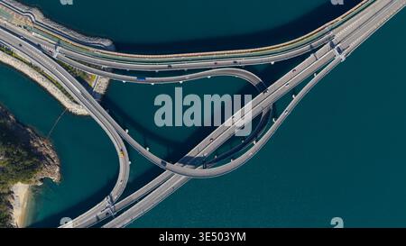 Aus der Vogelperspektive des Cross Bay Link Bridge Interchange mit geschwungenen Rampen und Verkehr über tiefblauem Wasser in New Territories, Hongkong. Stockfoto