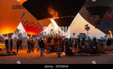 Bunte Heißluftballons, die mit Brennern aufgeblasen wurden, Touristen und Crew versammelten sich bei Sonnenaufgang um Körbe in Luxor, Ägypten Stockfoto