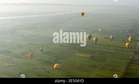 Farbenfrohe Heißluftballons, die bei Tagesanbruch über üppige grüne Felder und den Nil schweben, in Luxor, Ägypten Stockfoto