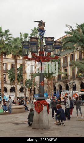 Kunstvoll gestalteter Lampenträger an der Plaza Reial, gotisches Viertel, Barcelona, Spanien, mit Palmen Gaudí, Arkadenhäuser und Touristen. Stockfoto