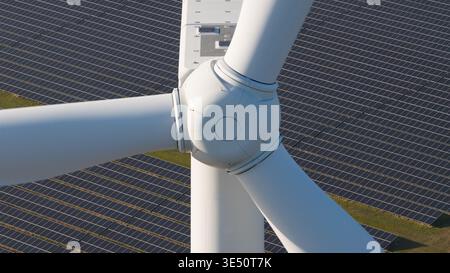 Luftaufnahme eines weißen Windturbinennetzes und der Rotorblätter, die über einer großen Reihe von Solarpaneelen positioniert sind. Stockfoto