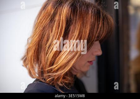 Frau mit schulterlangem braunem Haar und Highlights steht im Profil vor einem verschwommenen Hintergrund und zeigt eine moderne Frisur und natürliche Schönheit Stockfoto