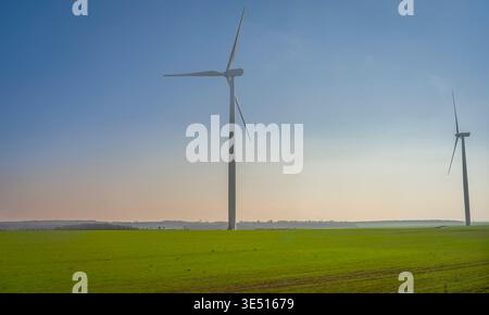 Paris, Frankreich - 03 19 2026: Panoramablick auf eine grüne Landschaft mit Windturbinen und blauem und orangefarbenem Himmel dahinter Stockfoto