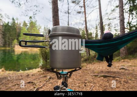 Nahaufnahme von kochendem Wasser in einem Metalltopf auf einem Gasherd auf einem Waldcamping in der Nähe eines Sees. Stockfoto