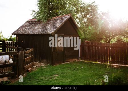 Blick auf das rustikale Holzhaus mit gekacheltem Dach, umgeben von einem Holzzaun und üppigem grünem Gras unter einer hellen Sonne, Sremska Mitrovica, Vojvodina, Serbi Stockfoto