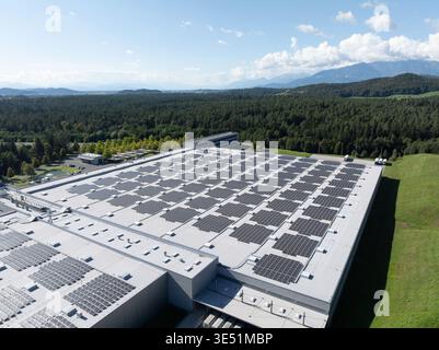 Aus der Vogelperspektive eines Logistikzentrums mit Lagerhäusern, Laderampen und Lkw, umgeben von grünen Feldern und Bergen. Stockfoto