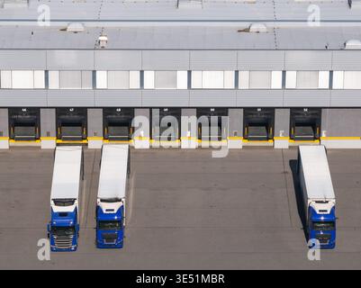 Ein Logistikzentrum mit Lagerhäusern, Laderampen und Lkw, die in einer belebten Umgebung auf das Be- oder Entladen warten. Stockfoto