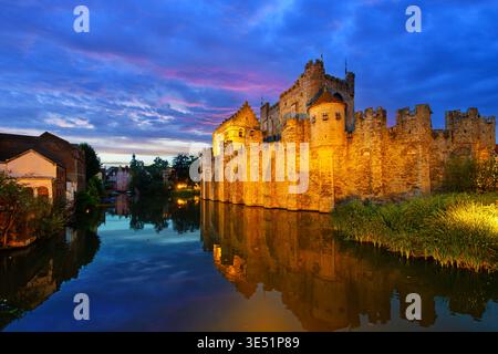 Abendlicher Blick auf das mittelalterliche Gravensteen-Schloss in der Dämmerung, das sich im Wassergraben in der historischen Altstadt von Gent, Belgien, spiegelt. Stockfoto