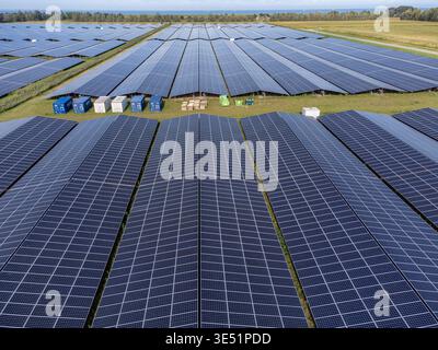 Aus der Vogelperspektive blitzende Sonnenkollektoren, die unter der Sonne leuchten und sich in Richtung Horizont erstrecken, mit aufgereihten Containern, Zonnepark Zuyderzon, Almere, F Stockfoto