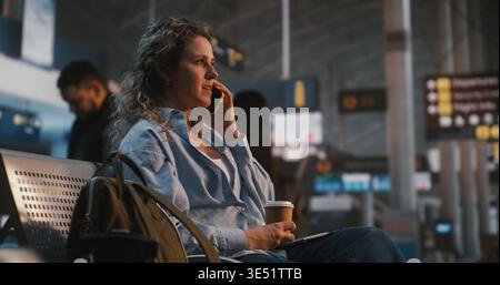 Die Junge Frau Sitzt Bequem In Der Airport Lounge Und Genießt Kaffee Bei Einem Fröhlichen Telefongespräch. Stressfreies Reiserlebnis, positive Emotionen und die Verbindung mit den Lieben. Stockfoto