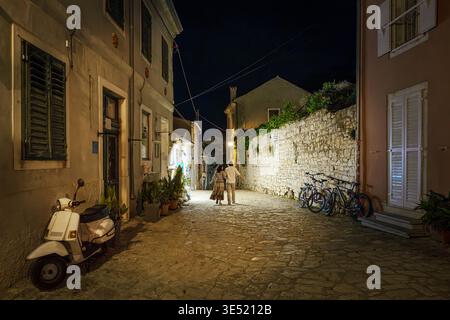Ein paar spazieren nachts durch eine enge kopfsteingepflasterte Gasse in der mittelalterlichen Altstadt der Küstenstadt Rovinj, Kroatien. Stockfoto