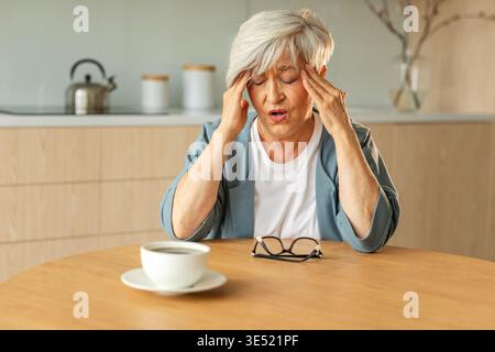 Kopfschmerzen. Unglückliche Seniorin mittleren Alters, die an Kopfschmerzen leidet, die sich zu Hause an den Schläfen reiben. Reife alte Großmutter berührt Schläfe und erlebt Stress Frau fühlt Schmerzen im Kopf Stockfoto