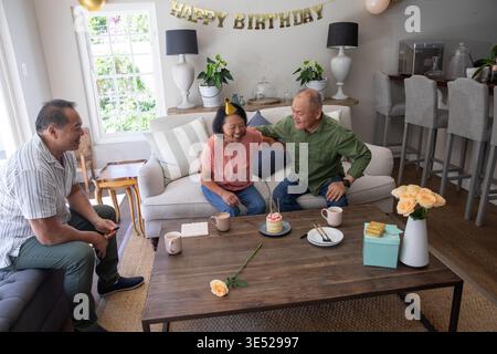 Asiatisch-chinesische Familie feiert zu Hause Geburtstag mit einer älteren Frau, die Partyhut und Kuchen trägt Stockfoto