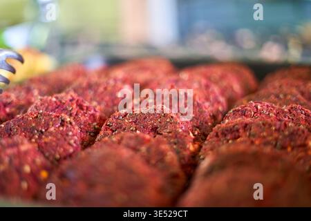 Nahaufnahme mehrerer roher Hamburger-Patties, die in ordentlichen Reihen angeordnet sind und ihre satte rote Farbe und sichtbare Würze von schwarzem Pfeffer und zeigen Stockfoto