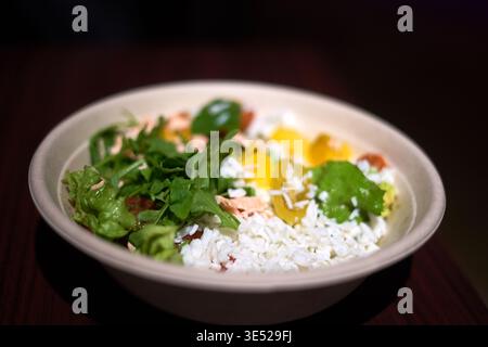 Ein Nahfoto einer Schüssel mit frischen Lebensmitteln, die in einem hellen, umweltfreundlichen Einwegbehälter serviert wird. Die Schüssel enthält verschiedene bunte Farben Stockfoto