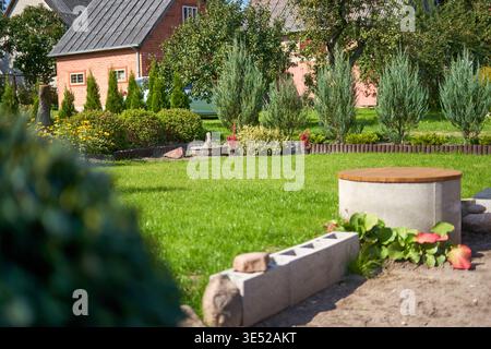 Ein gepflegter Wohngarten mit einem üppig grünen Rasen im Vorder- und Hintergrund. Im rechten Vordergrund befindet sich ein runder Beton Stockfoto