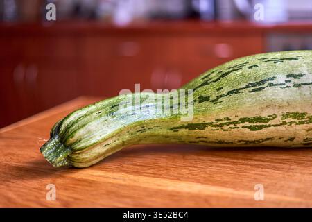 Nahaufnahme einer frischen, lang gestreckten Zucchini oder Kürbis mit markanten grünen und weißen Streifen auf einem hölzernen Schneidebrett Stockfoto