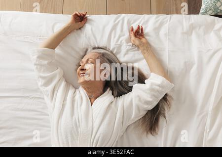 Lächelnde ältere Frau, die mit geschlossenen Augen auf dem Bett liegt und den Morgen genießt Stockfoto