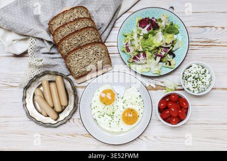 Teller mit Spiegeleiern, Brot, Salat, Wurst und Quark auf braunem Holztisch, Kopierplatz. Stockfoto
