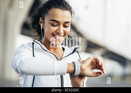 Lächelnde Frau, die ihre körperliche Aktivität auf Smartwatch überprüft. Junge Sportlerin, die während des Trainings auf Aktivitätstracker blickt Stockfoto