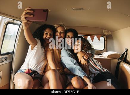 Vier schöne Freunde machen Selfie in einem Van während eines Roadtrips. Lächelnde Frauen im Urlaub Stockfoto