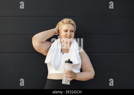 Lächelnde und große Frau, die an der Wand steht. Positive Frau, die sich nach dem Training und der Haaranpassung entspannt Stockfoto
