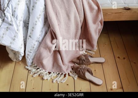 Pinkfarbene Decke und Wildleder-Slips auf Holzboden. Skandinavischer Lebensstil. Entspannen Sie sich Stockfoto