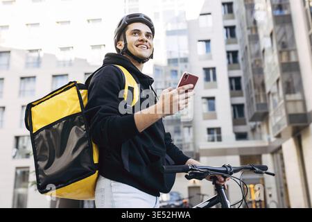 Porträt der Geburt Mann mit einem Mobiltelefon, trägt thermische Rucksack stehen gegen Wohngebäude Stockfoto
