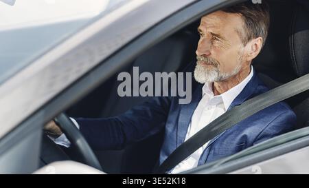 Seitenansicht eines Reifen Geschäftsmannes. Senior männlich, der sich beim Autofahren auf die Straße konzentriert Stockfoto